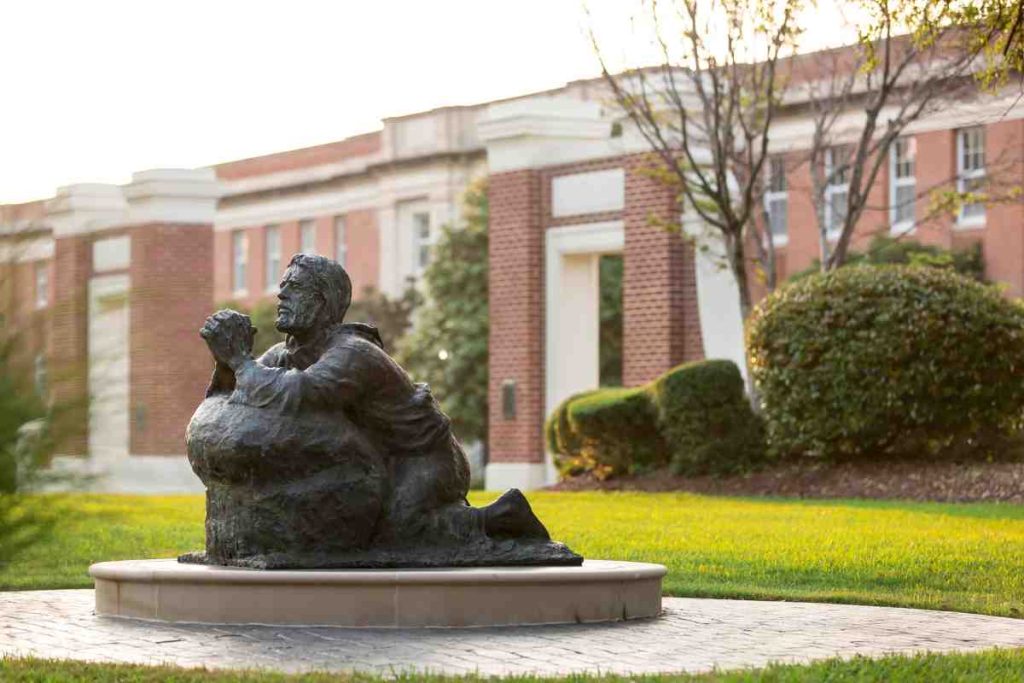 Jesus kneeling in prayer near a campus courtyard statue